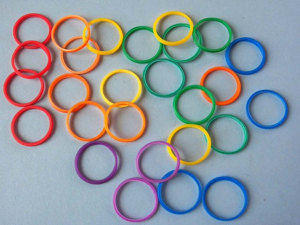 Small rubber rings in red, orange, yellow, green, blue and purple scattered on a pale blue surface.